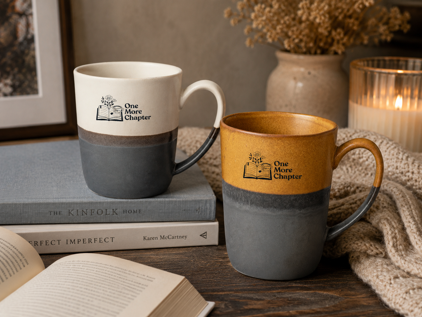 Two mugs with 'One More Chapter' branding on a wooden surface with books and a candle.