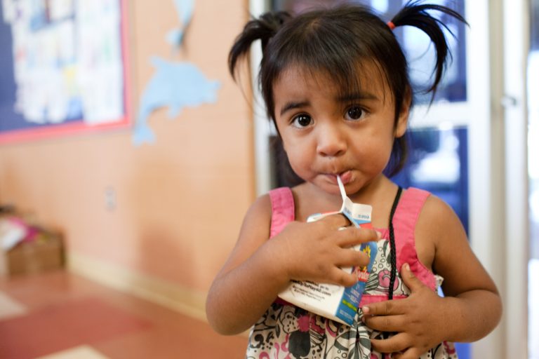 A child sipping from a milk carton provided by No Kid Hungry
