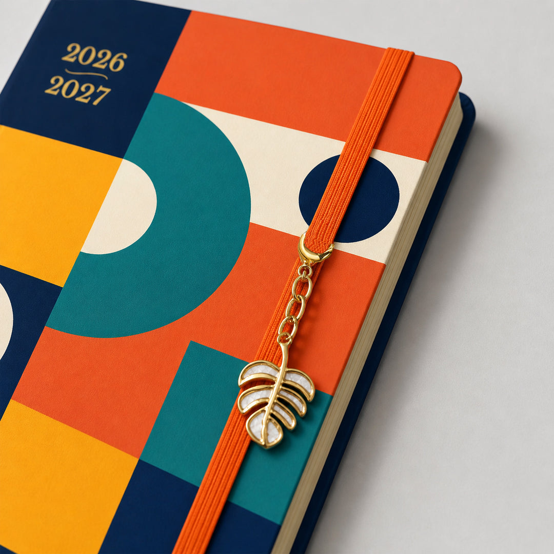 Colorful planner with a decorative leaf charm on a light gray background 