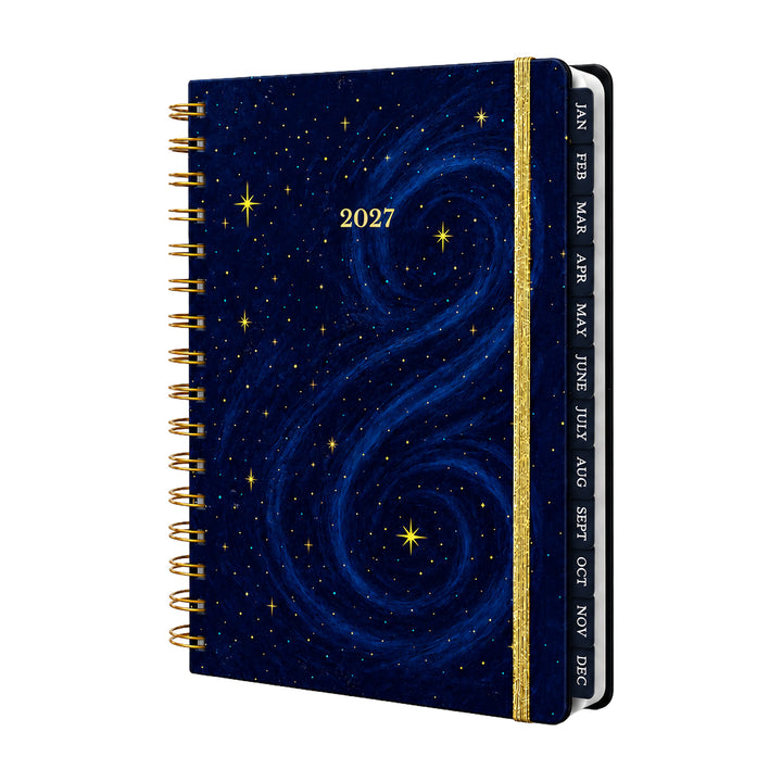 A 2027 spiral-bound planner with a deep blue galaxy night-sky cover, featuring gold stars and a gold glitter spine band with monthly tabs labeled JAN through NOV. 