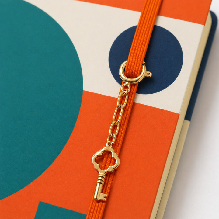 Gold key charm on an orange ribbon against a colorful geometric background 