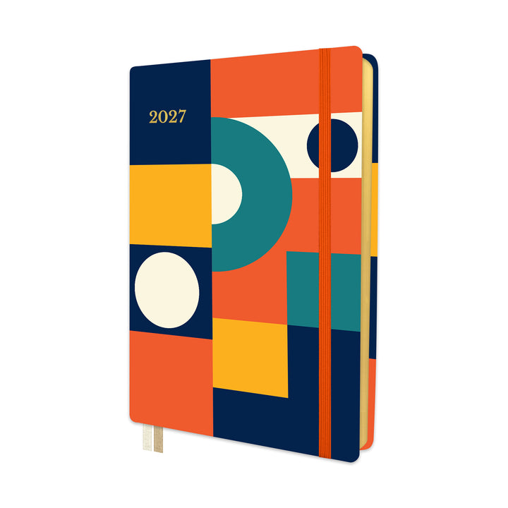 A 2027 hardcover planner with a colorful geometric cover design in orange, navy, yellow, teal, and cream, featuring an orange elastic closure band and ribbon bookmarks. 