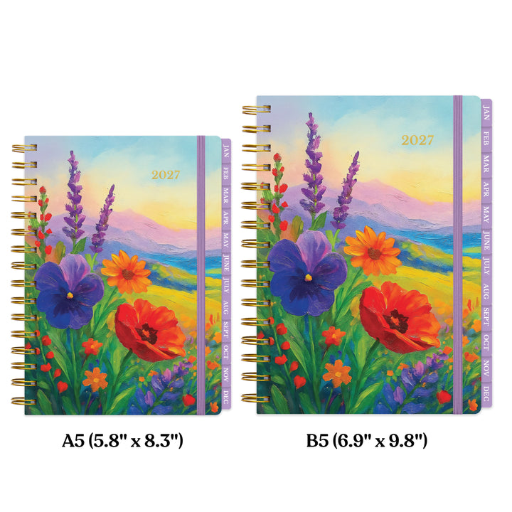 Size comparison between spiral-bound planner with a colorful painted wildflower landscape cover, shown upright on a white background. The cover features purple pansies, red poppies, lavender, and yellow flowers over blue and green hills under a pastel sky. 