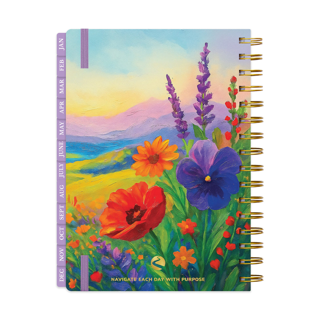A spiral-bound daily planner or journal with a colorful painted wildflower landscape cover, shown upright on a white background. The cover features purple pansies, red poppies, lavender, and yellow flowers over blue and green hills under a pastel sky. 