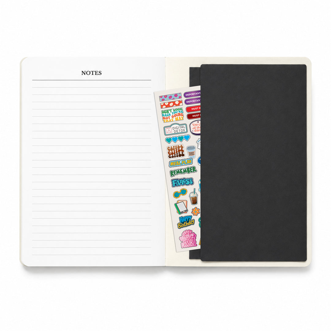 Notebook with lined pages, a black cover, and a sheet of stickers on a white background 