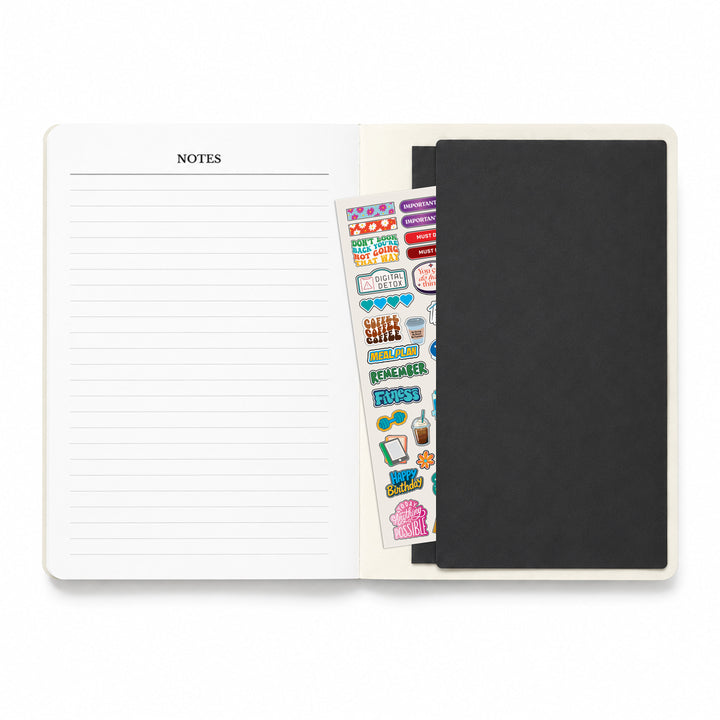 Notebook with lined pages, a black cover, and a sheet of stickers on a white background 