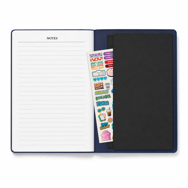 Open notebook with lined pages, a black cover, and a sheet of colorful stickers on a white background. 