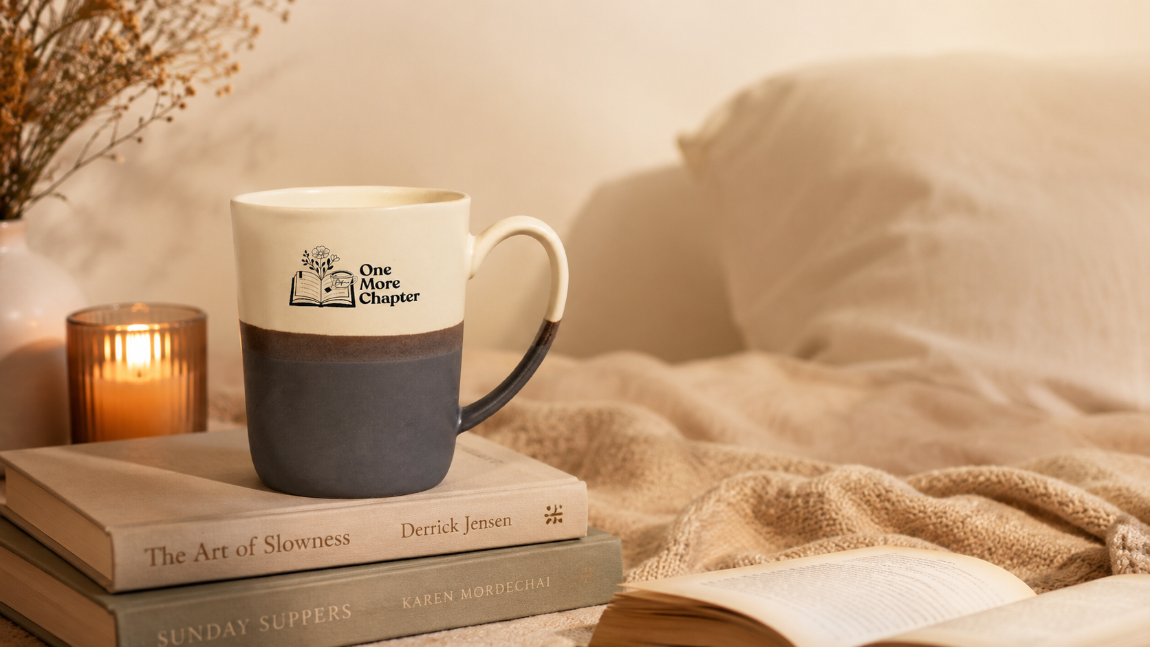 Mug with a logo on a stack of books next to a candle and blanket